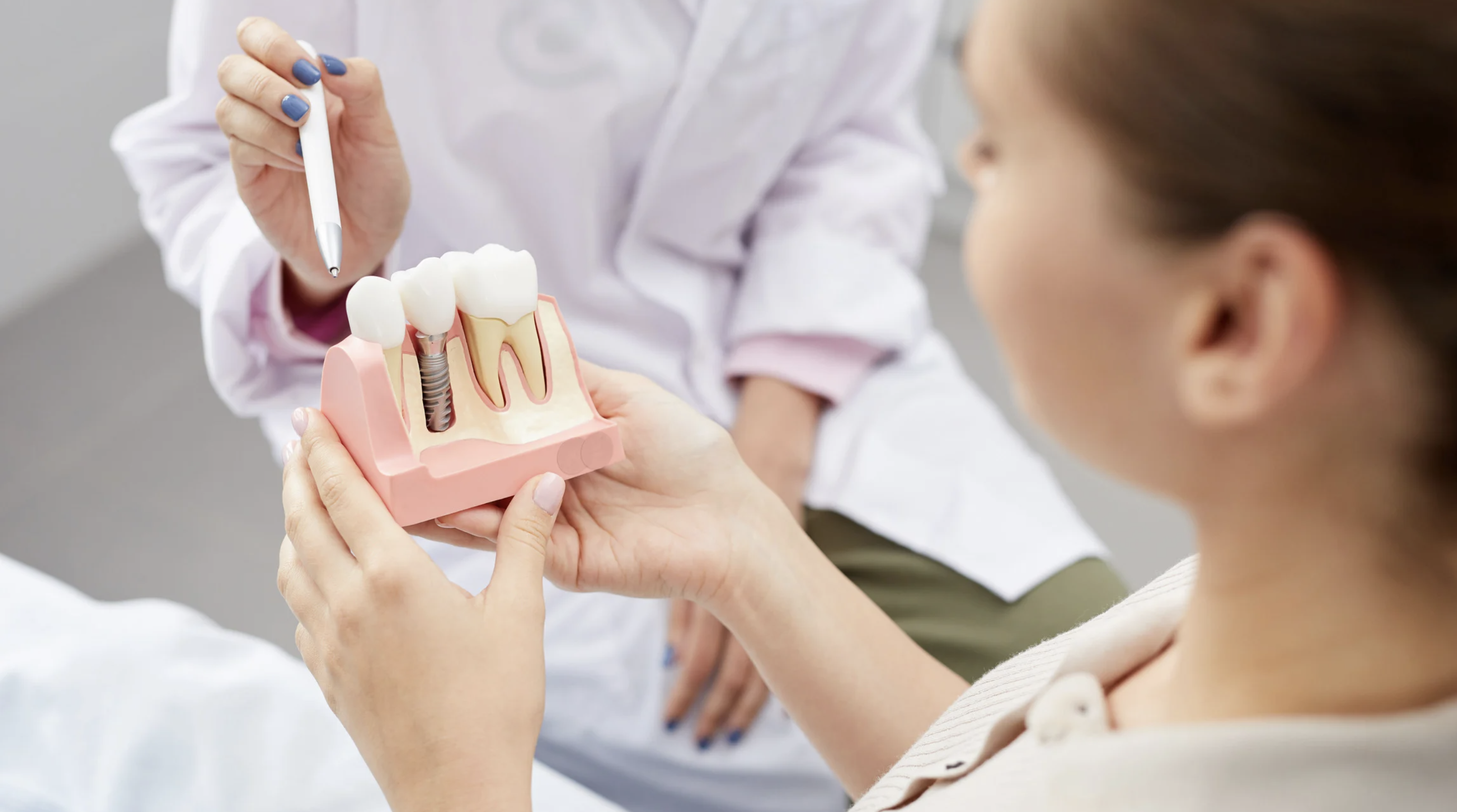 Doctor showing female patient a dental implant model made of different materials in a clinic in Bangkok.