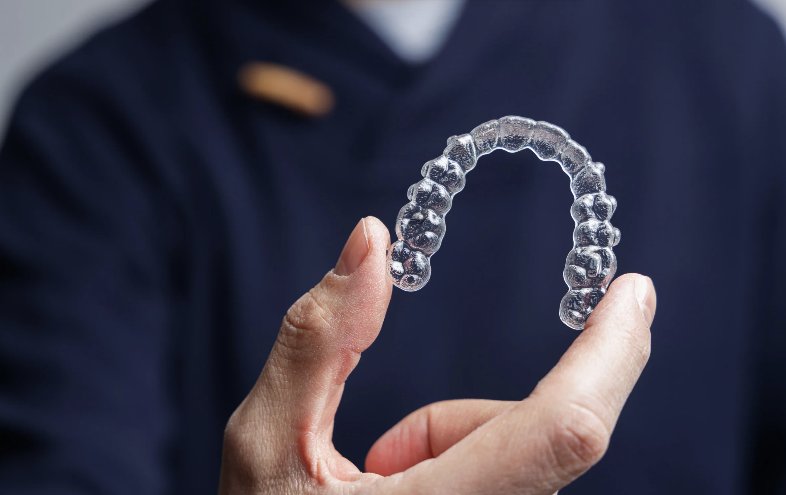 Woman holding a pair of clear Invisalign aligners and smiling in a dental clinic in Bangkok