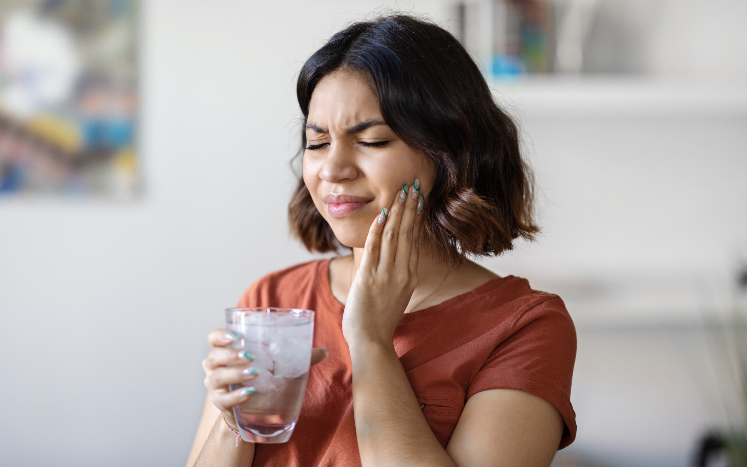 A woman with teeth sensitive to cold water winces in pain