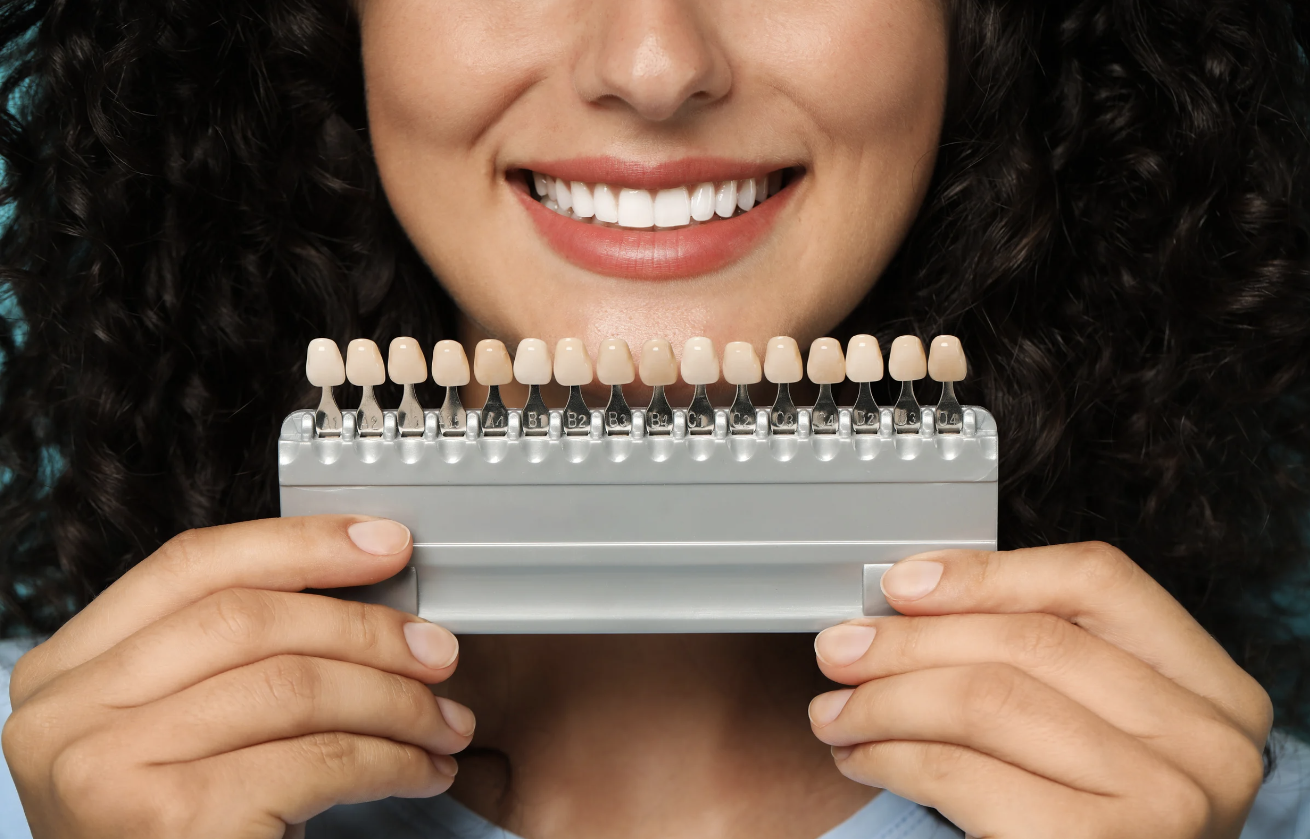 A smiling woman with a set of tooth color samples for veneers